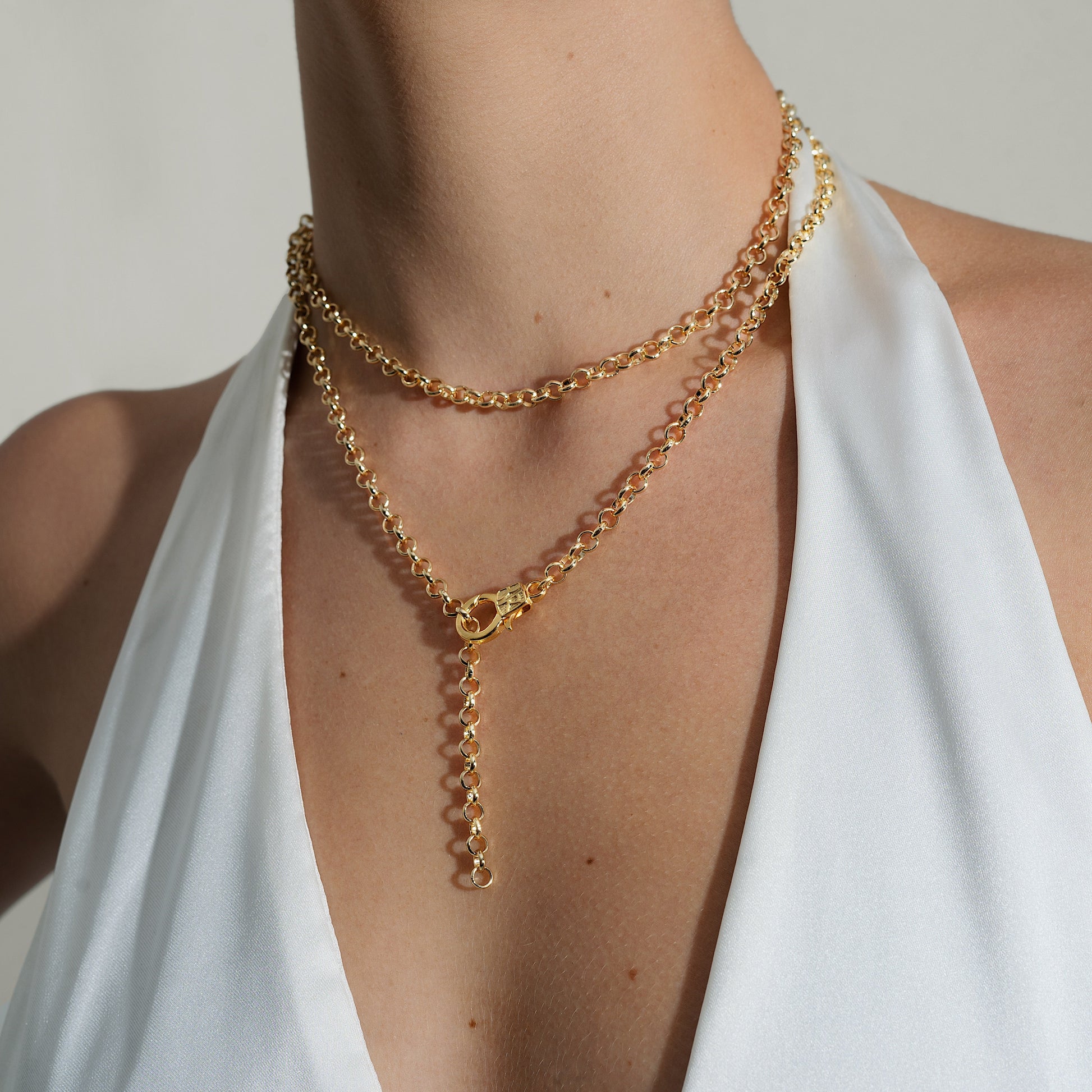Gold chain necklace worn by a person in a white top against a neutral background