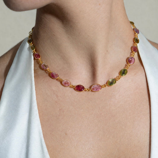 Necklace with multicolored gemstones and gold chain on a person wearing a white top.