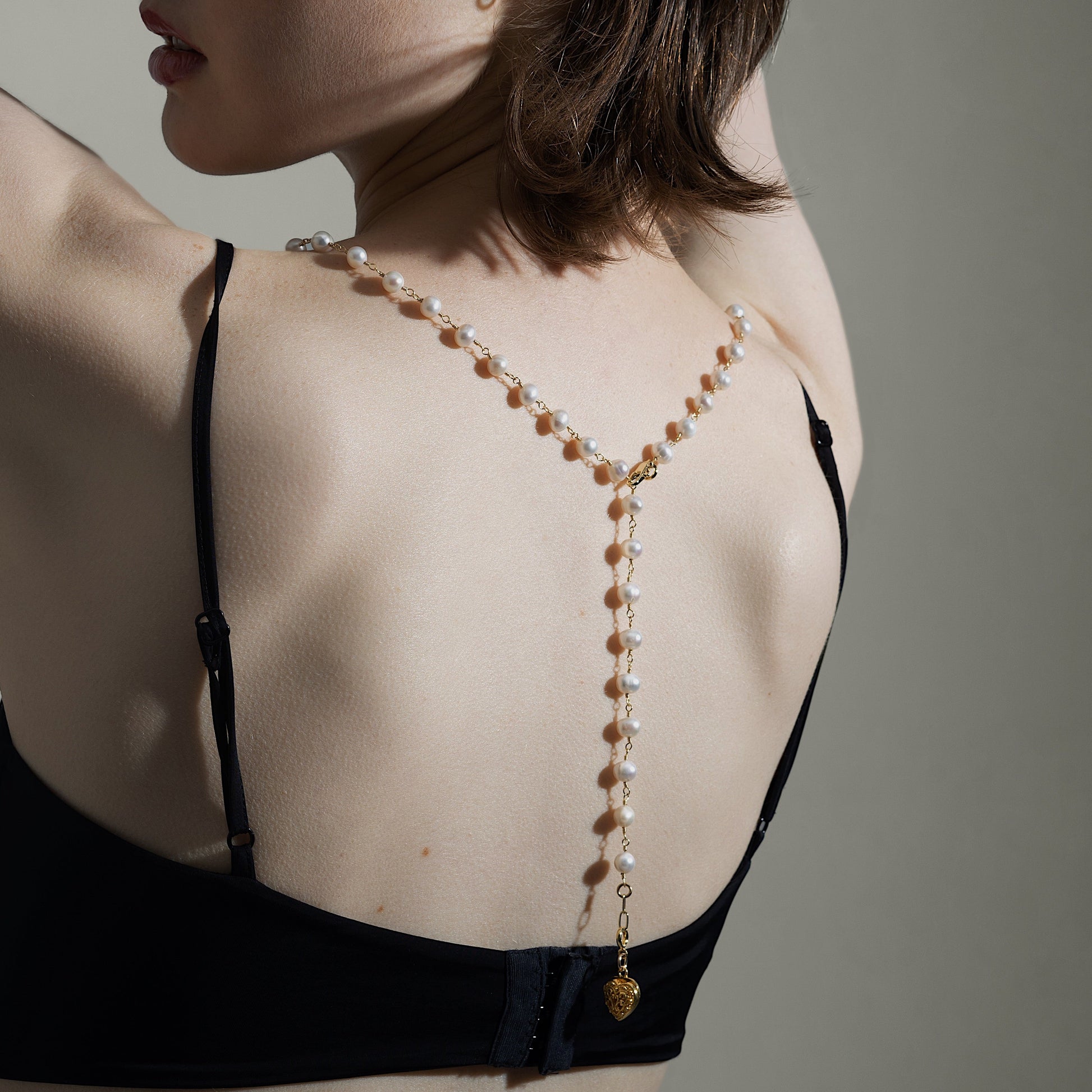 Woman wearing a black strappy top with a beaded necklace against a neutral background