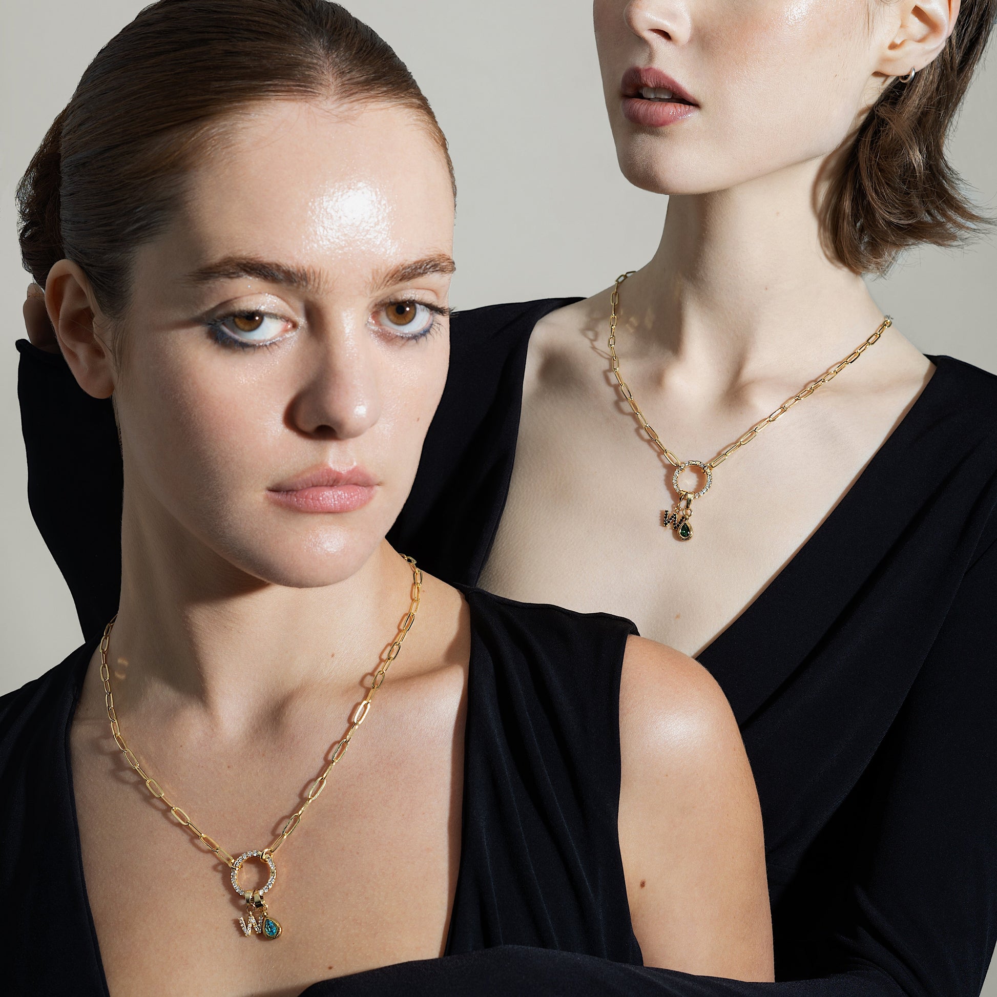 Two women wearing gold necklaces against a neutral background