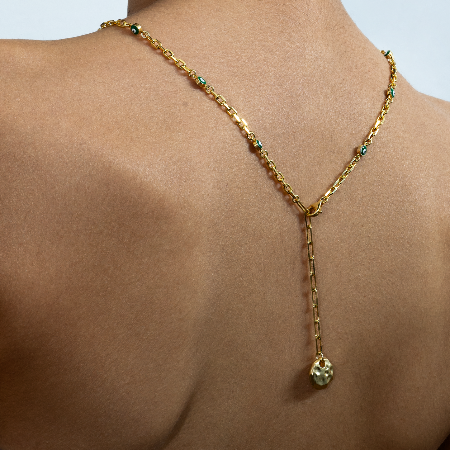 Gold necklace with a pendant on a person's neck against a light background