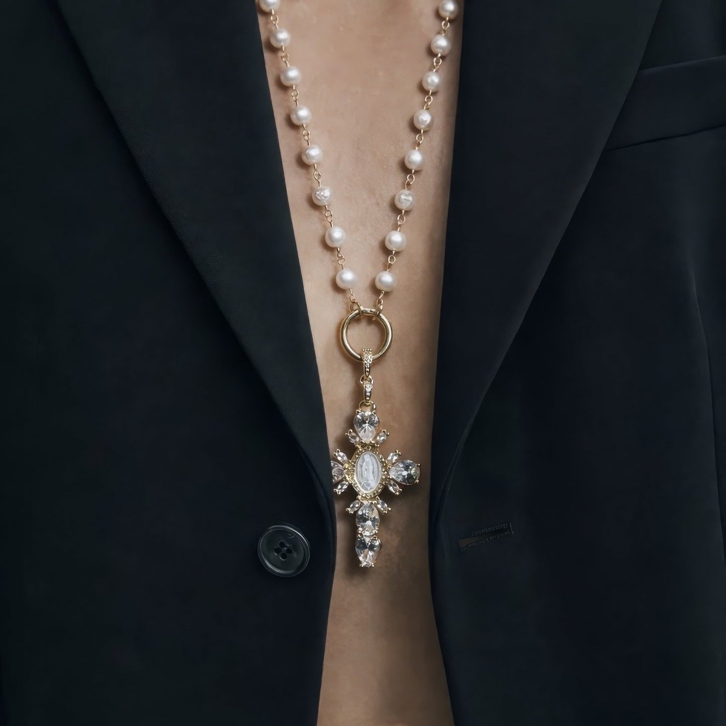 Pearl necklace with a cross pendant worn by a person in a black coat.