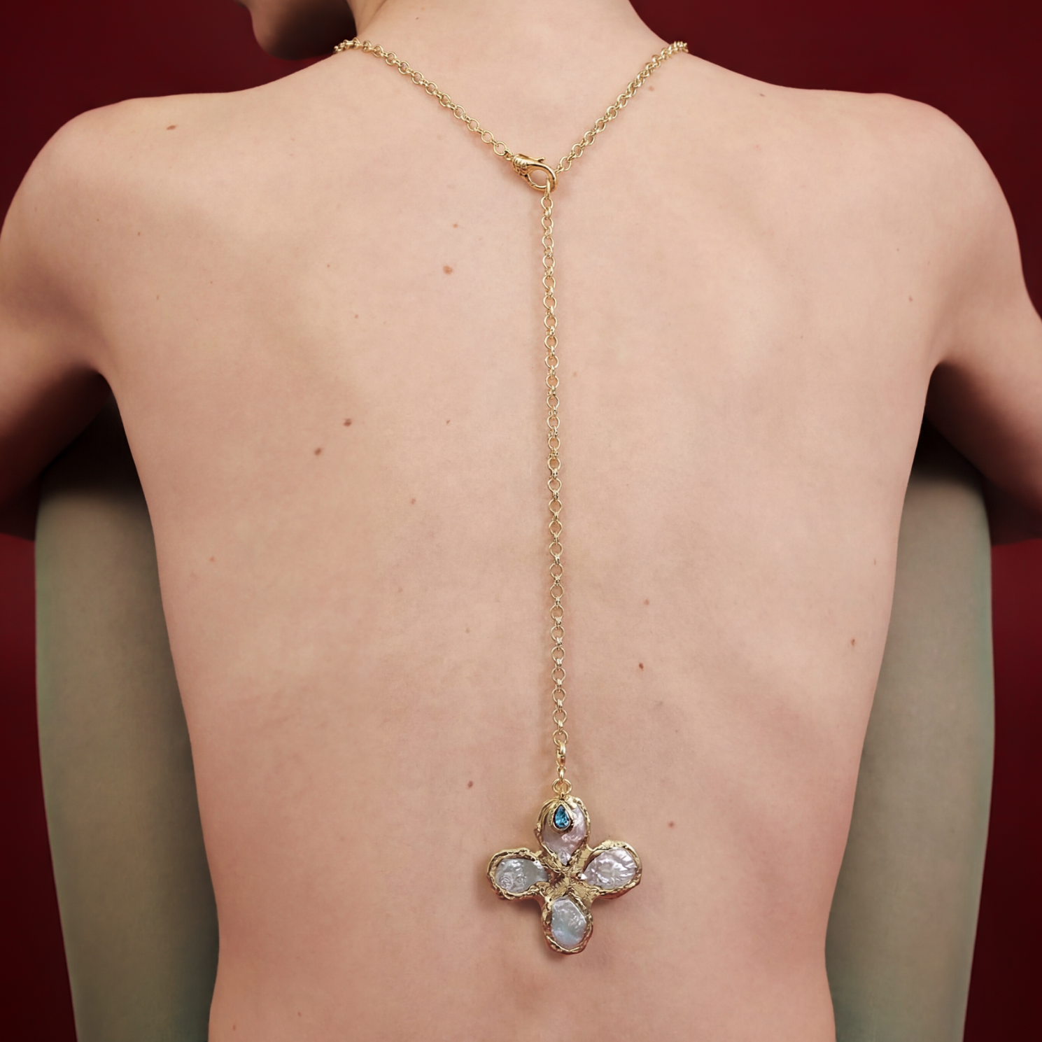 Gold necklace with a floral pendant on a person's back against a red background