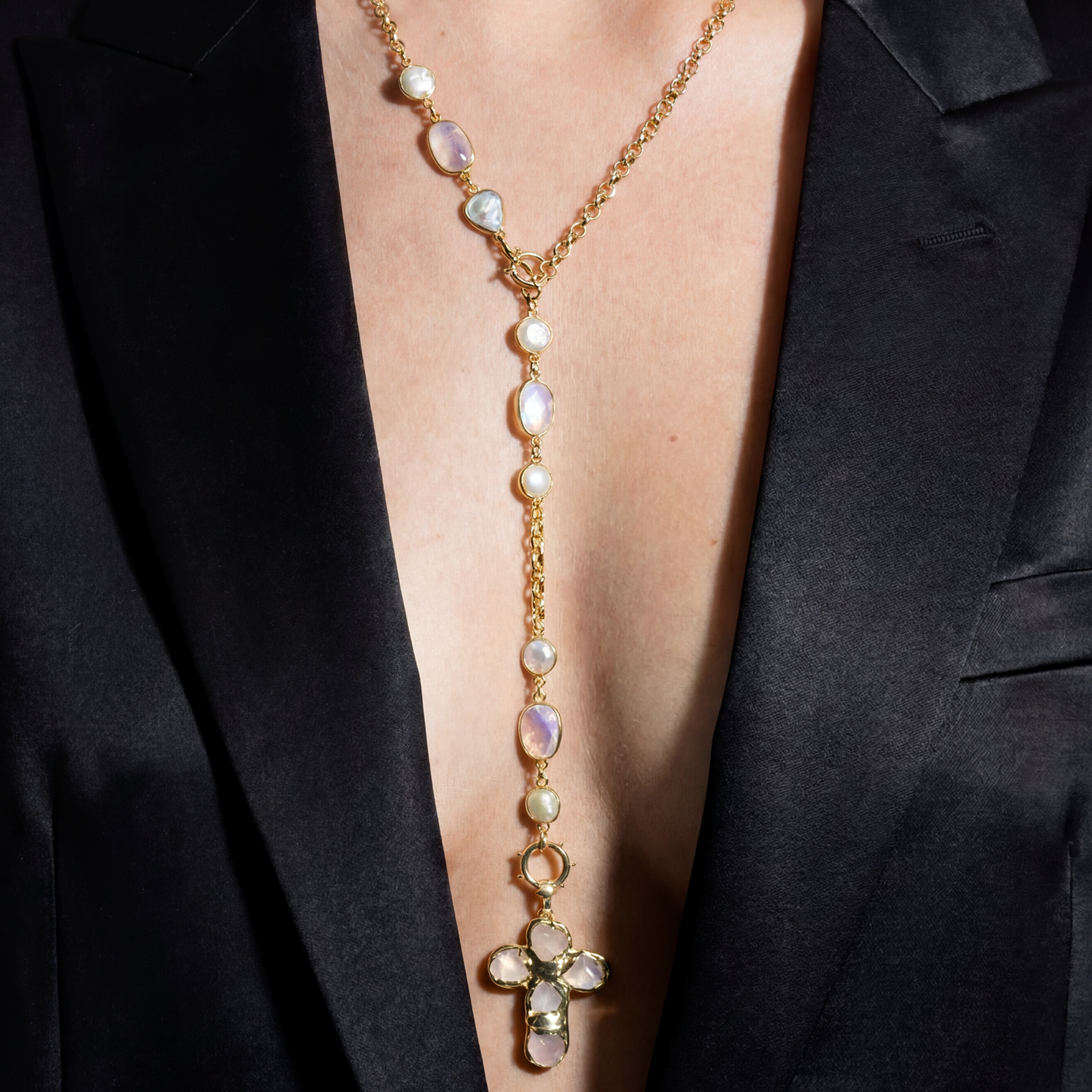 Gold necklace with beads and a cross pendant on a black blazer.