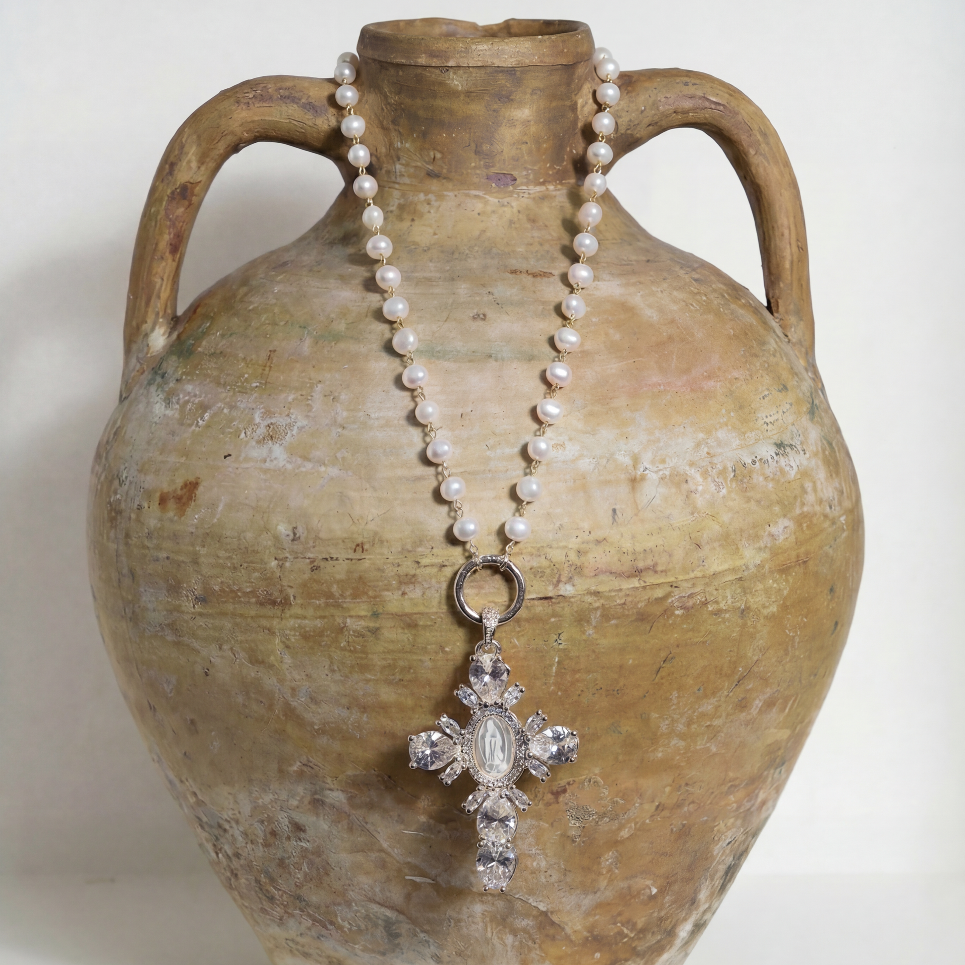 Pearl necklace with a cross pendant draped over an ancient vase.