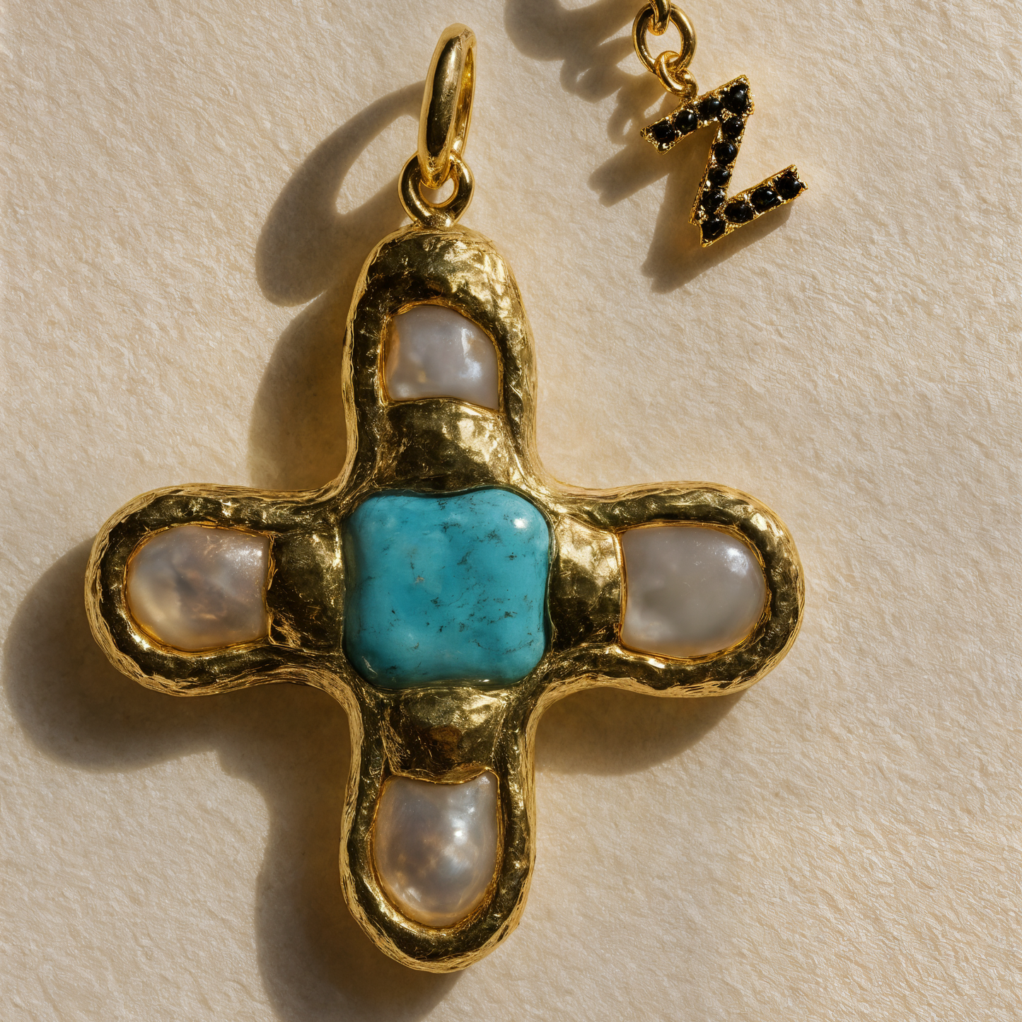 Gold cross pendant with turquoise center and pearl-like accents on a beige background