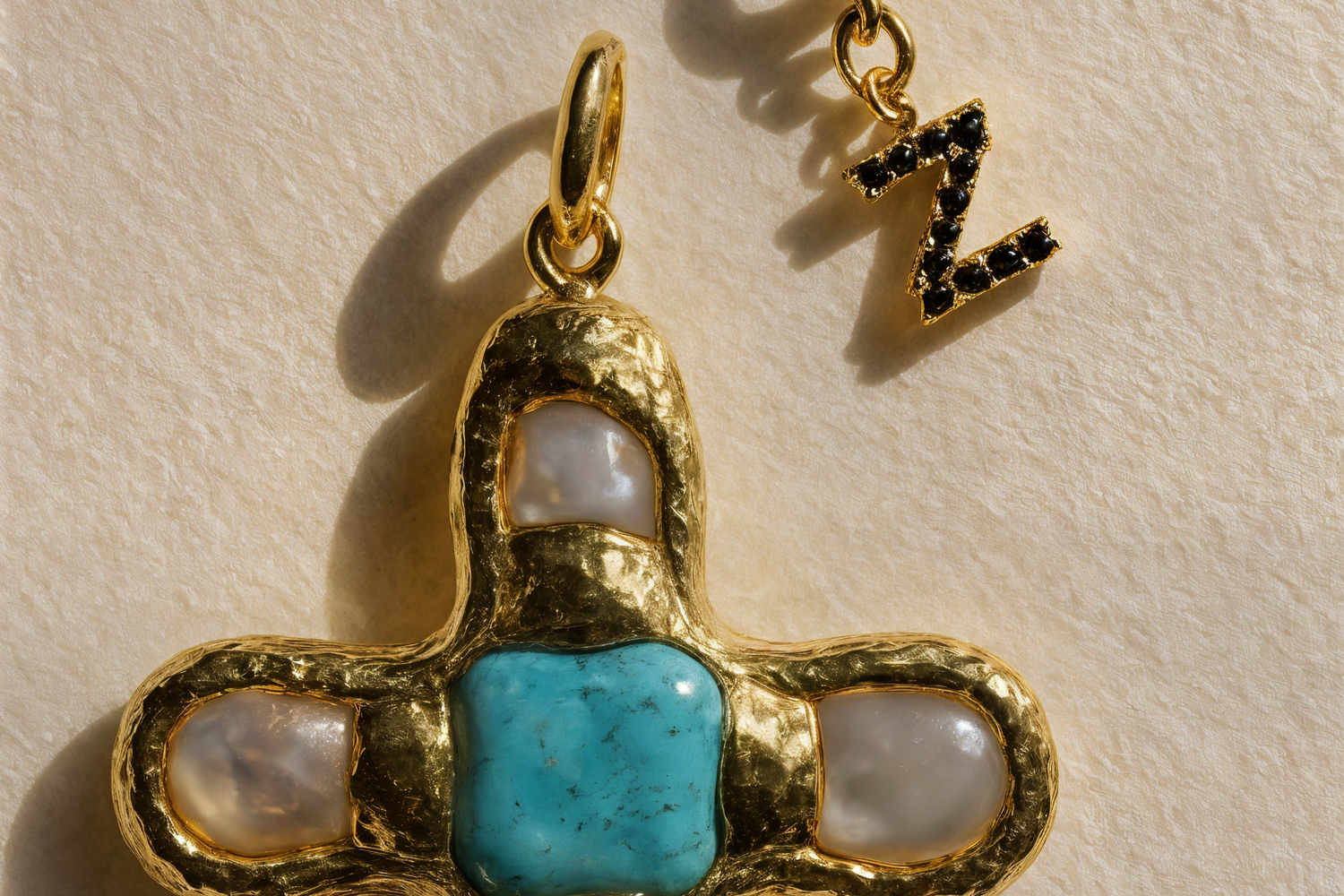 Gold cross pendant with turquoise center and pearl-like accents on a beige background